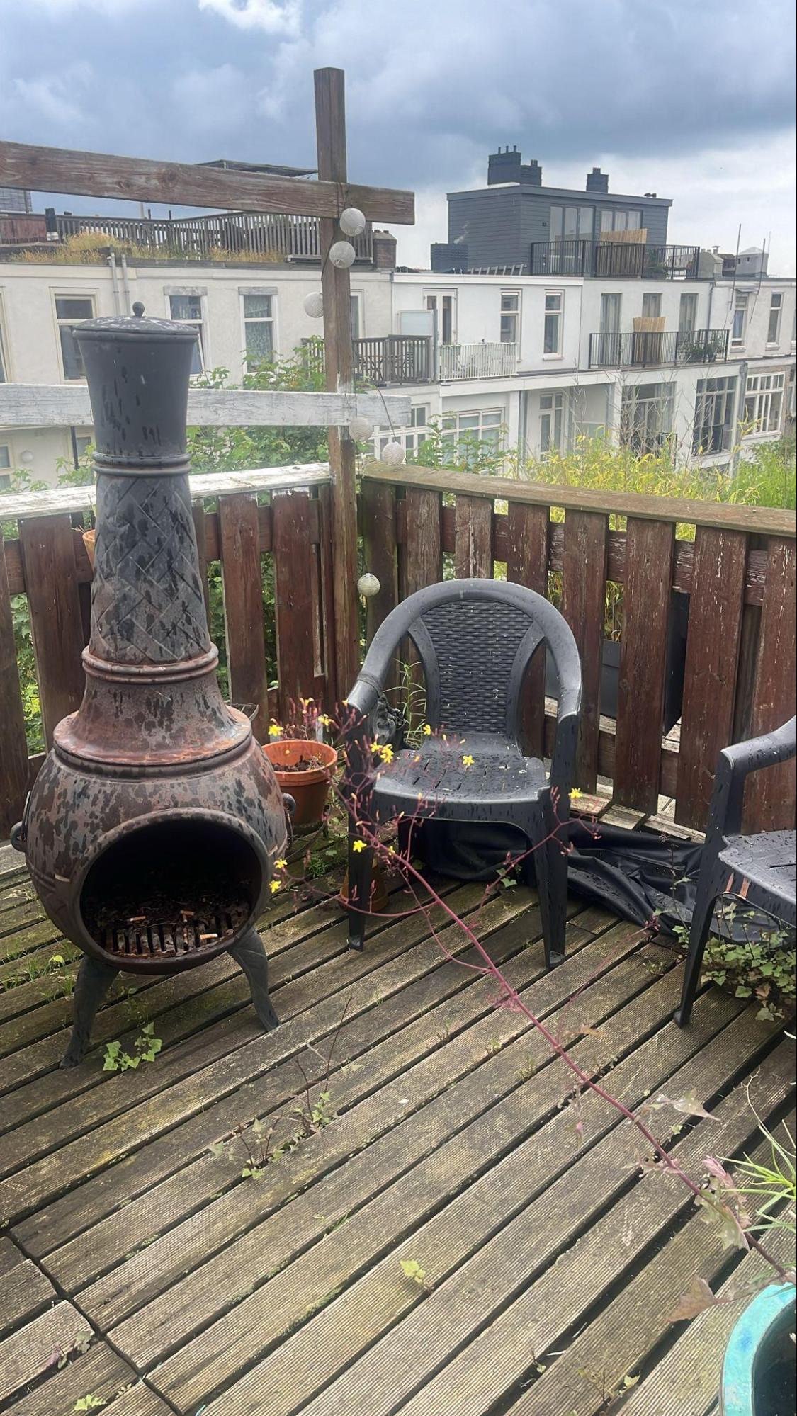 Houten dakterras met chimenea en plastic stoel met uitzicht op daken